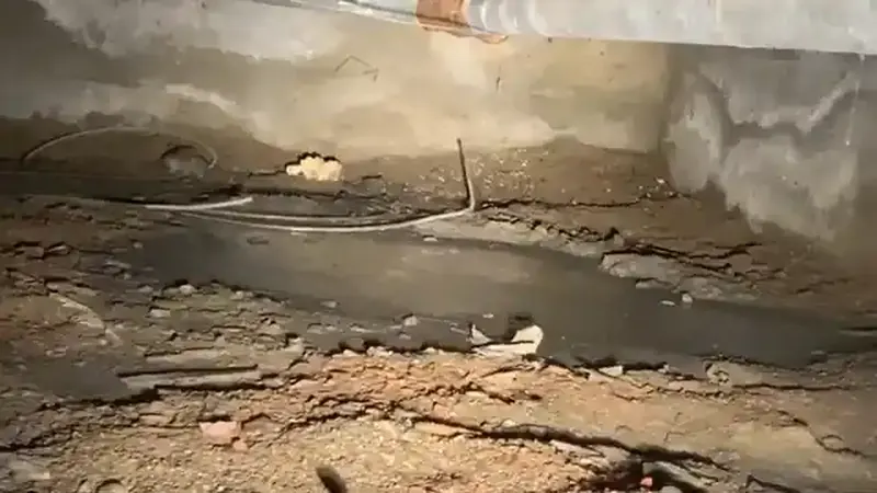 Unfinished crawlspace under a Commerce City home showing galvanized supply lines and vapor barrier
